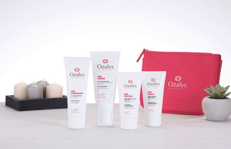 Trois bouteilles de cosmétiques sont posées sur une table à côté d'un sac rose.