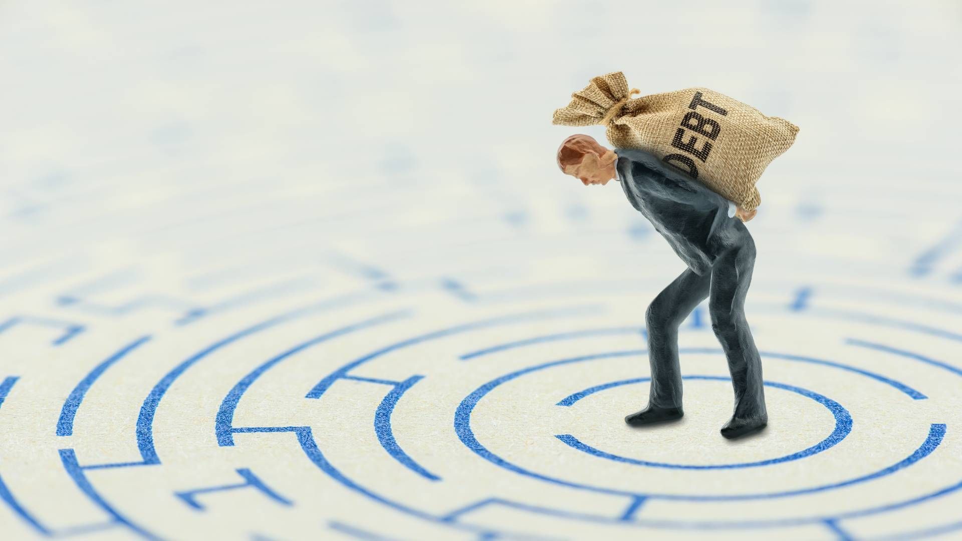 A miniature man is carrying a bag of debt in a maze.