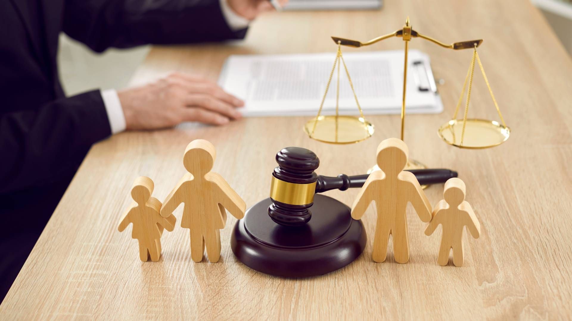 A wooden family is sitting on a wooden table next to a judge 's gavel and scales of justice.