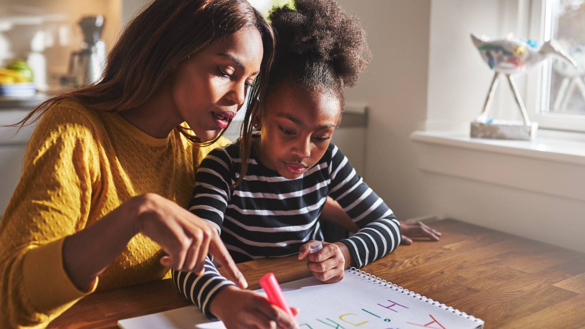 A woman is helping a little girl with her homework at a table.