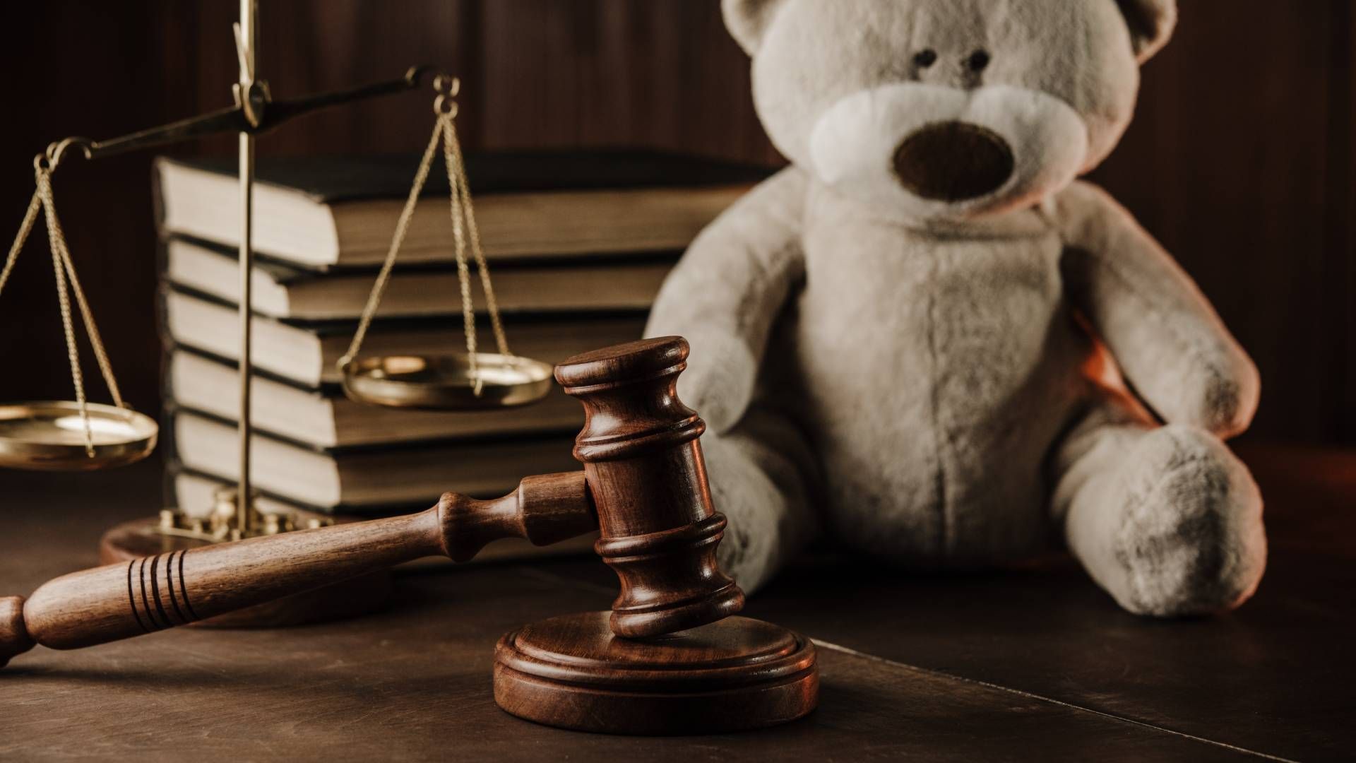 A teddy bear is sitting next to a wooden gavel and scales of justice.