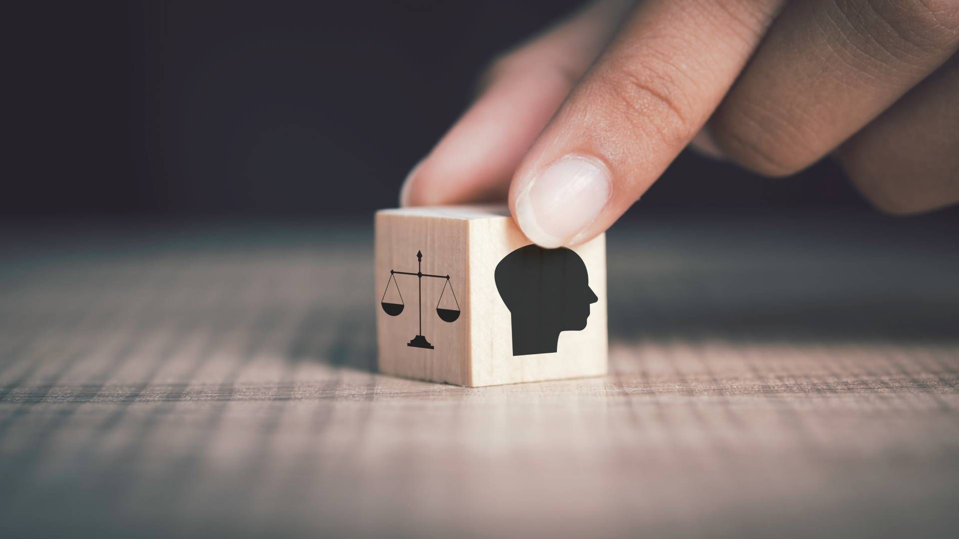 A person is holding a wooden block with a silhouette of a head and scales of justice on it.