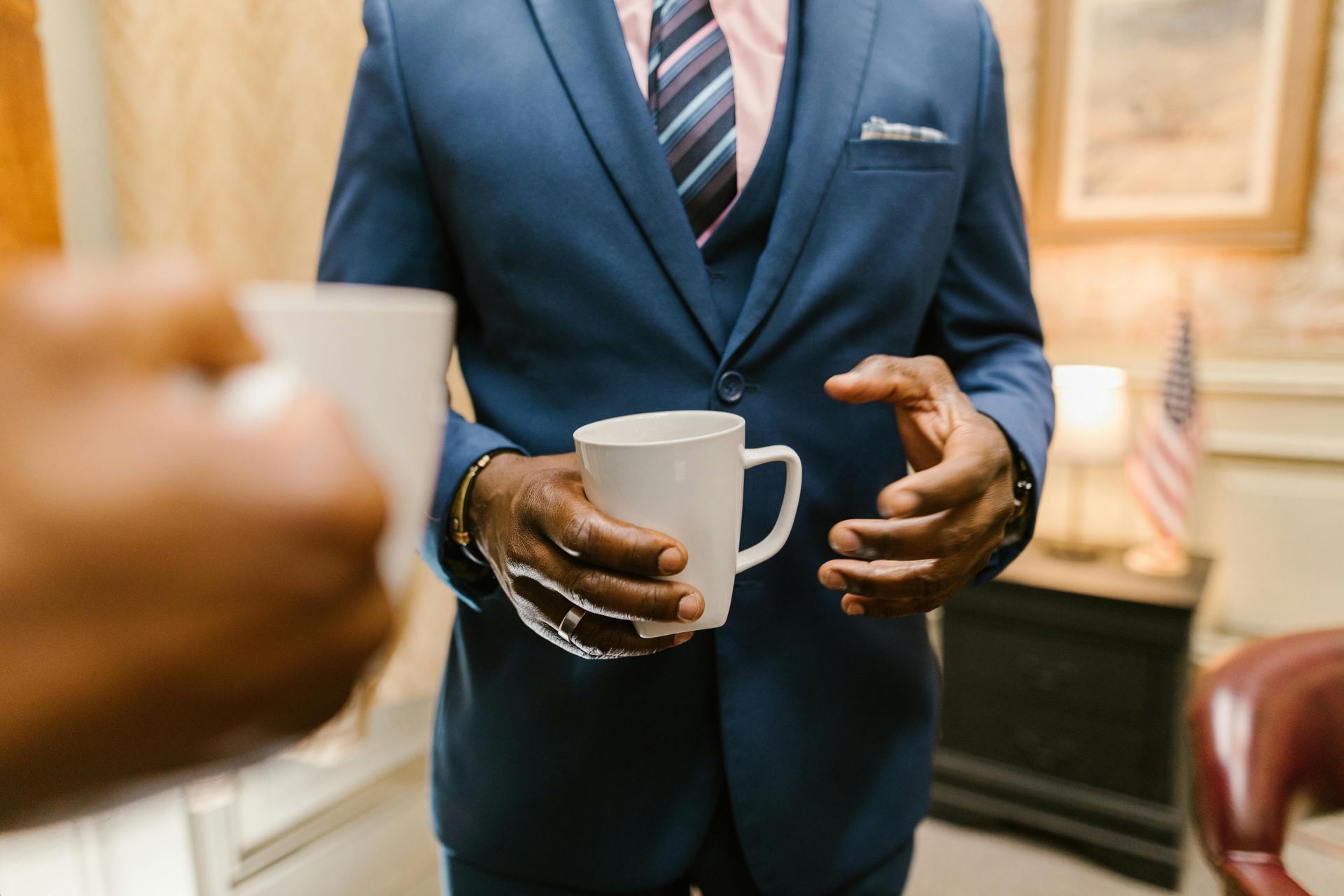 A man in a suit and tie is holding two cups of coffee.