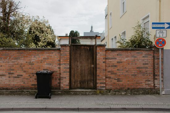 Brick wall with wooden door, black trash bin, and street signs.