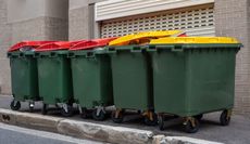 Green trash bins with red and yellow lids on a sidewalk.