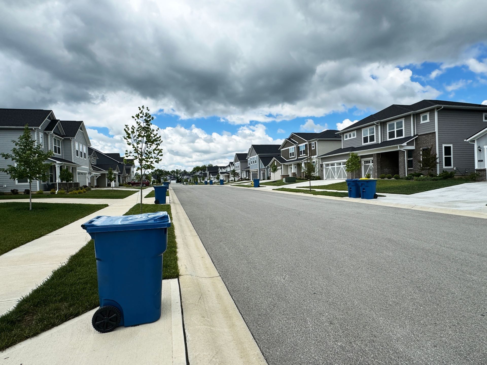 A street lined with houses on a cloudy day, blue trash cans in front.