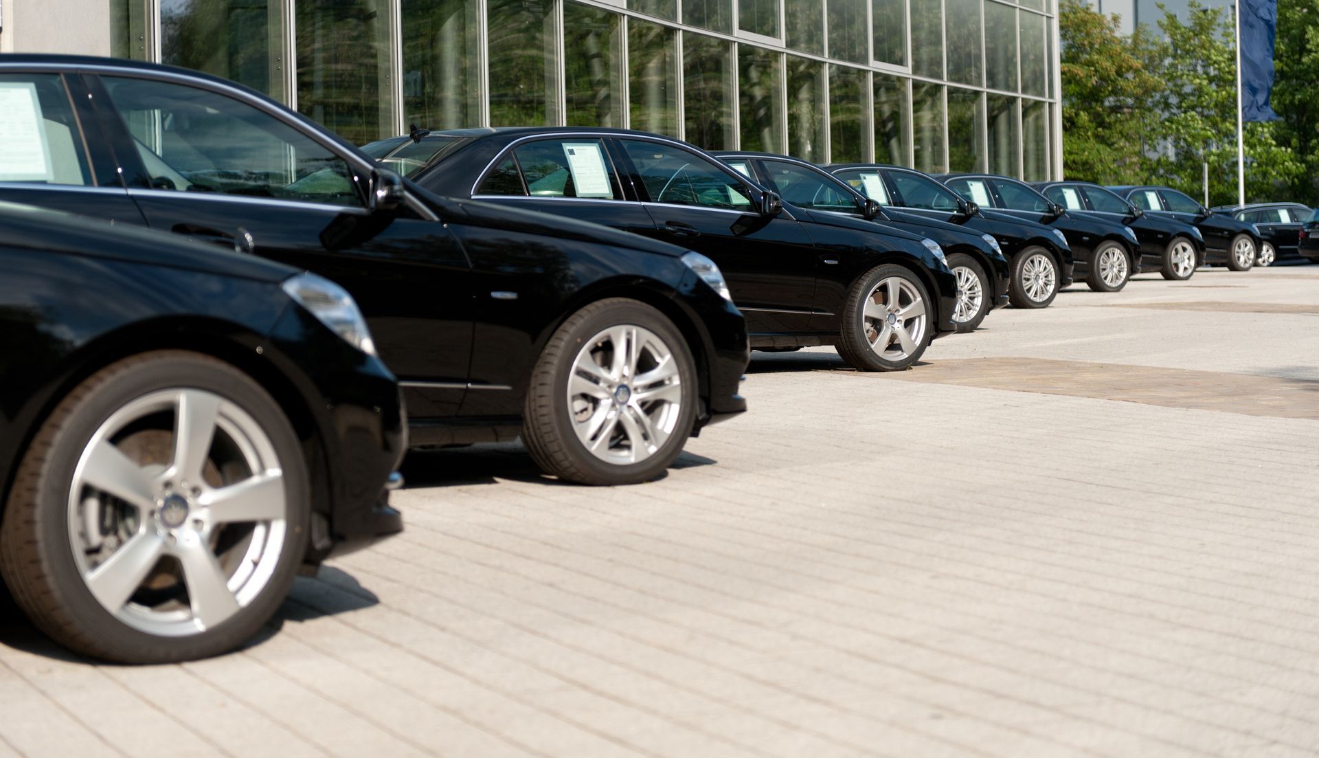 Row of parked black cars outside a glass-fronted building on a paved lot
