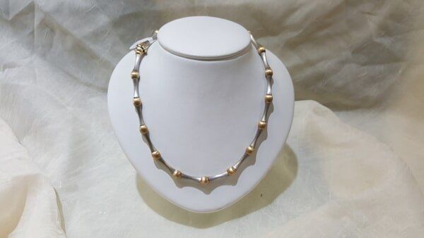 A gold and silver necklace is on a white mannequin