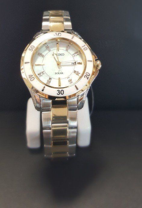 A silver and gold watch is sitting on a white stand