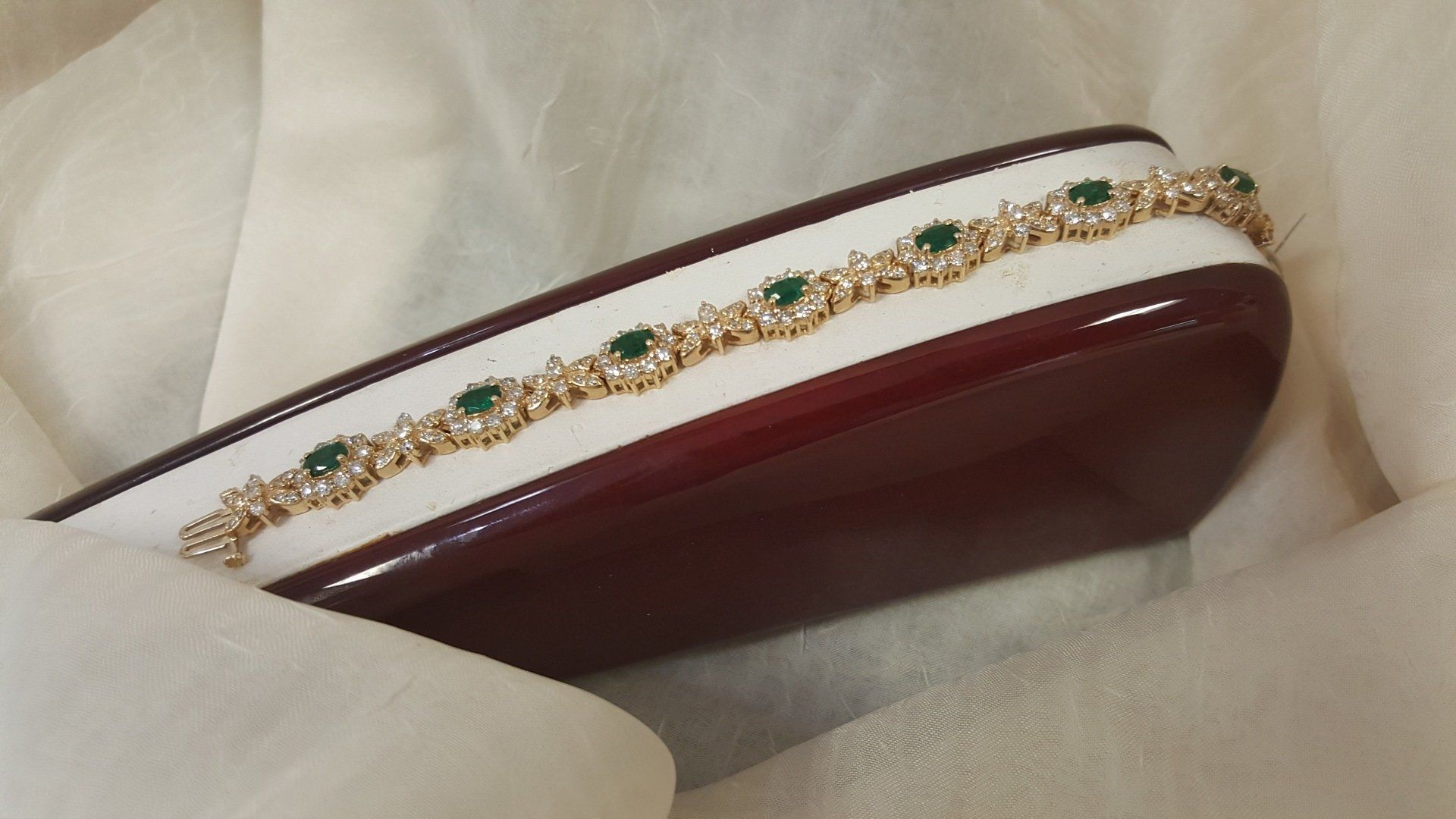 A bracelet with emeralds and diamonds on a white cloth