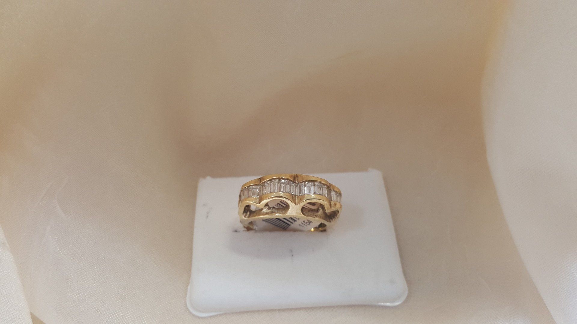 A gold ring with diamonds is sitting on a white display case.