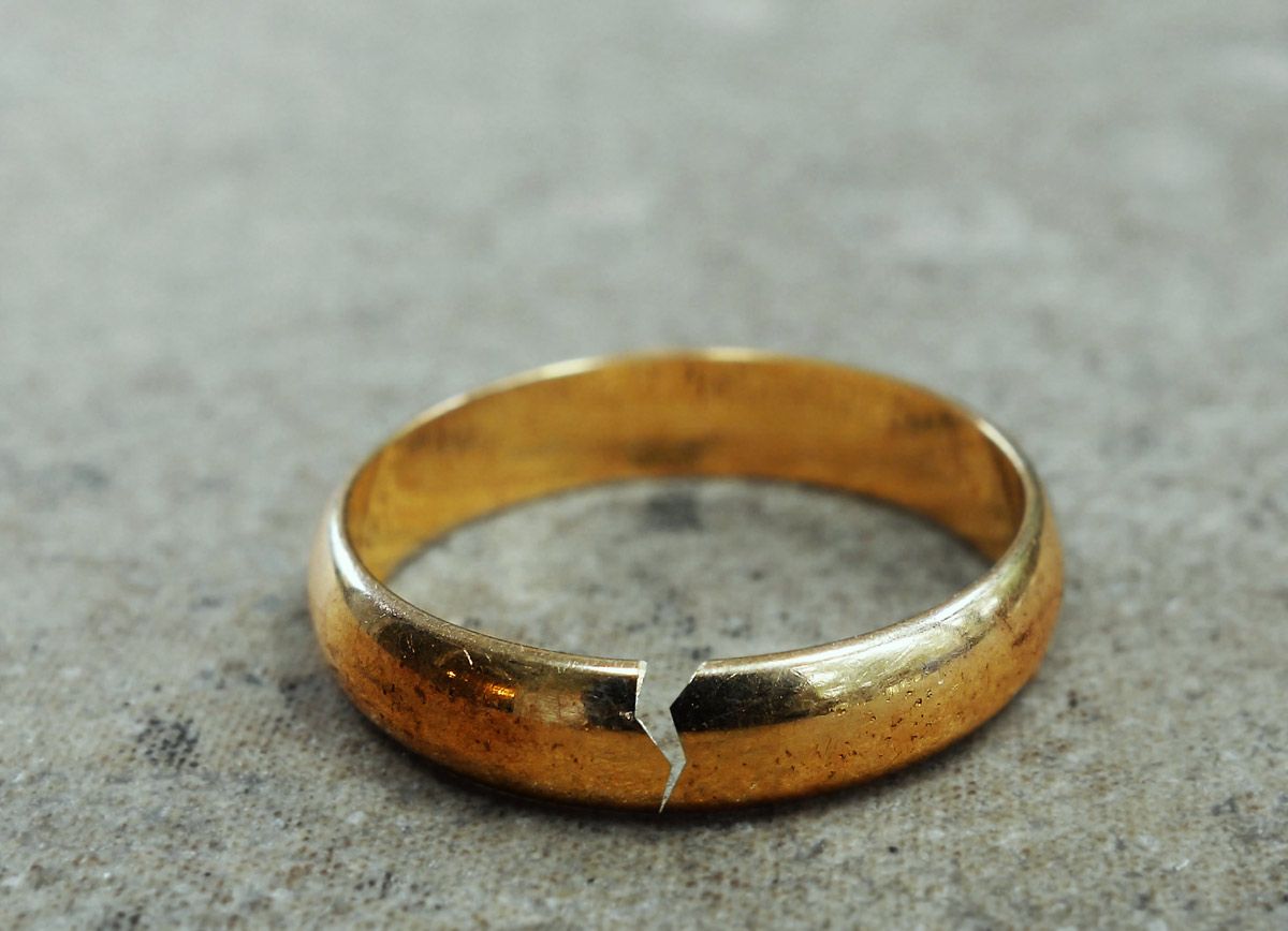 A broken gold wedding ring is sitting on a concrete surface