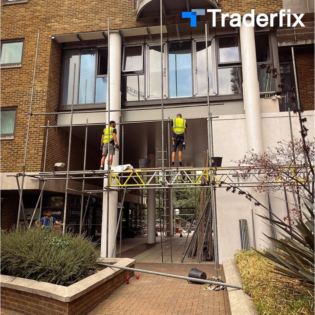 Two men are standing on a scaffolding in front of a building.