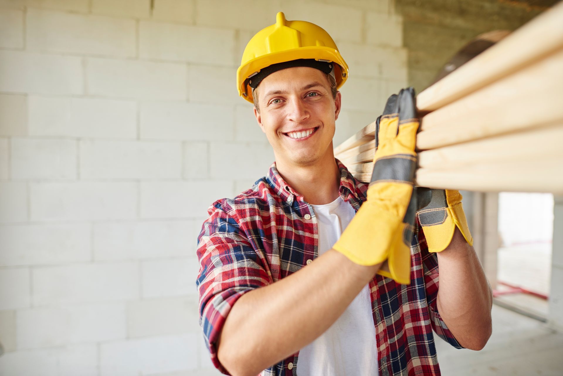 A man wearing a hard hat and gloves is carrying a stack of wood.