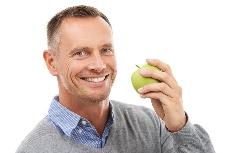 A man is holding a green apple in his hand and smiling.