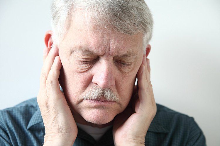 An older man with a mustache is holding his ears because he has a headache.