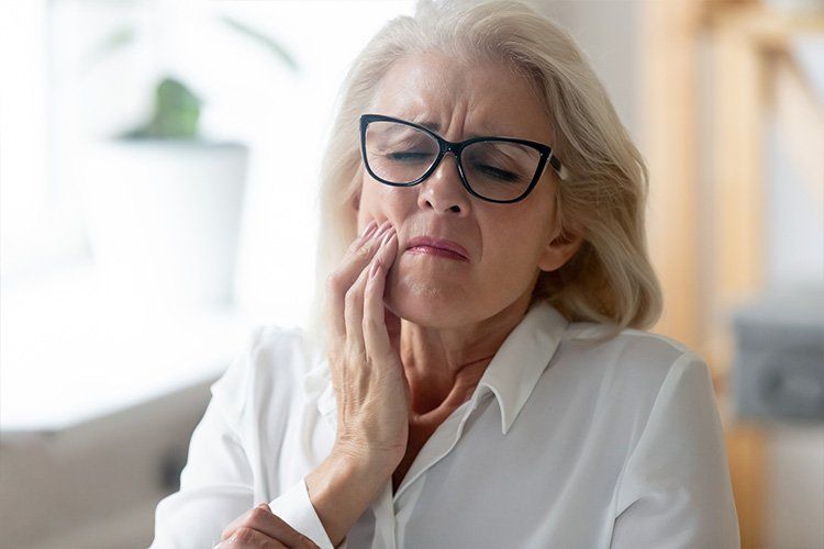 An older woman wearing glasses is holding her mouth in pain.