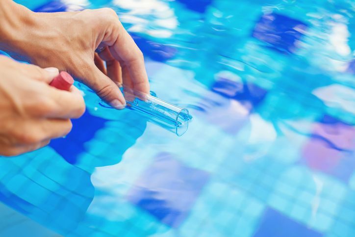 Close-up of hands performing swimming pool water treatment, by taking water sample to a flask.