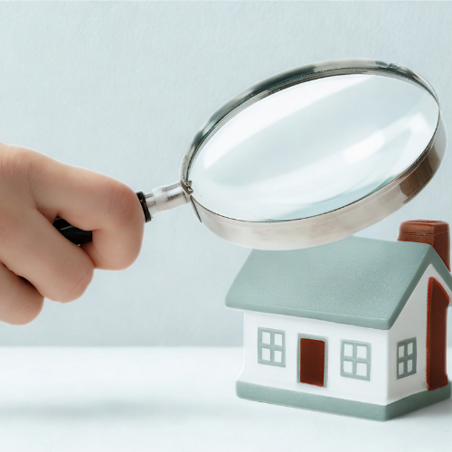 Hand holding magnifying glass over miniature house.