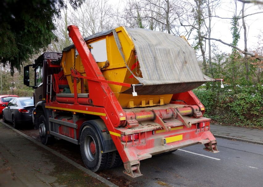 A Red and Yellow Dumpster Truck is Parked on the Side of the Road — Totally Skip Bins in Veresdale, QLD