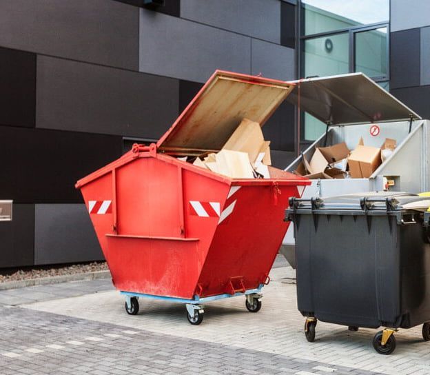 A Red Dumpster is Sitting Next to a Black Dumpster — Totally Skip Bins in Cedar Vale, QLD