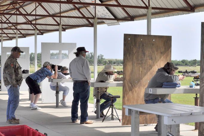 People shooting rifles at an outdoor gun range with a roof.