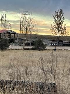 A sunset over a dry grass field with a house in the background.