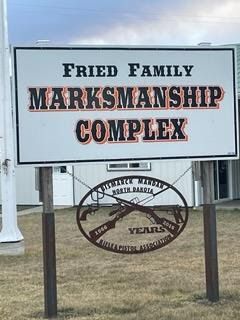 A sign for the fried family marksmanship complex is sitting in front of a building.