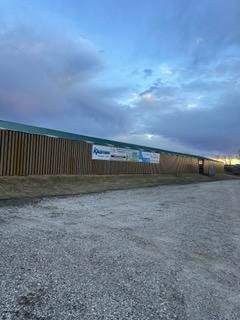 A large wooden building with a green roof is sitting on top of a gravel road.