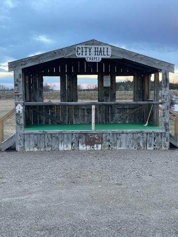 A small wooden building called the city hall is sitting on top of a dirt field.