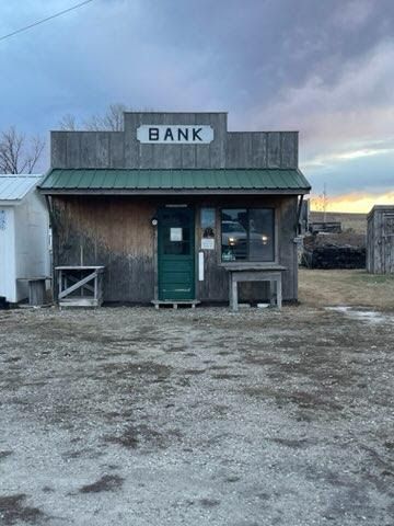 A small wooden bank building in the middle of a dirt field.
