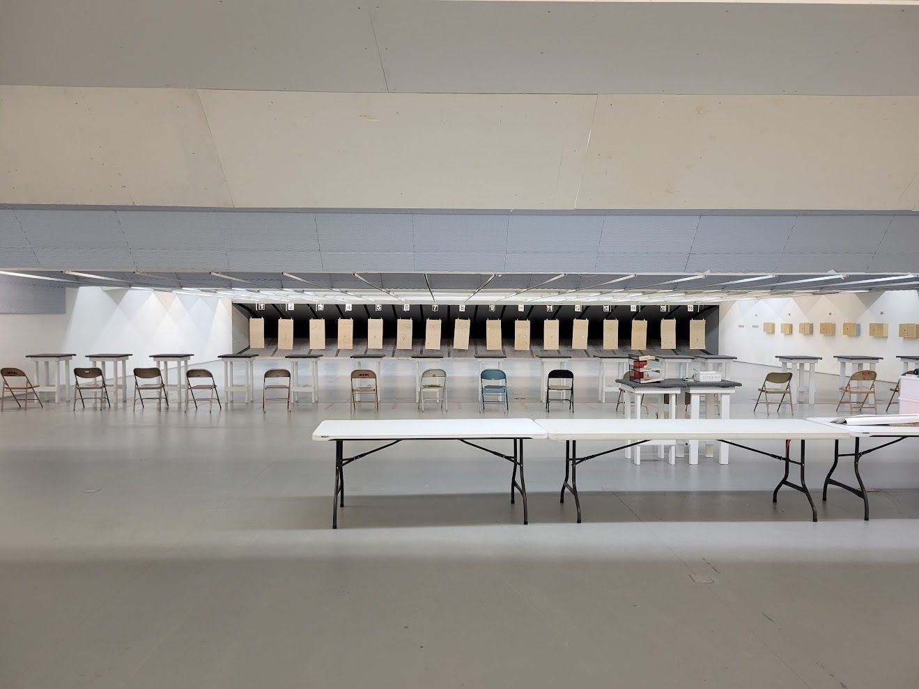 Empty indoor shooting range with target backstops, chairs, and tables.