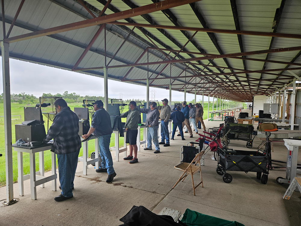 People shooting rifles at an outdoor range under a covered structure.