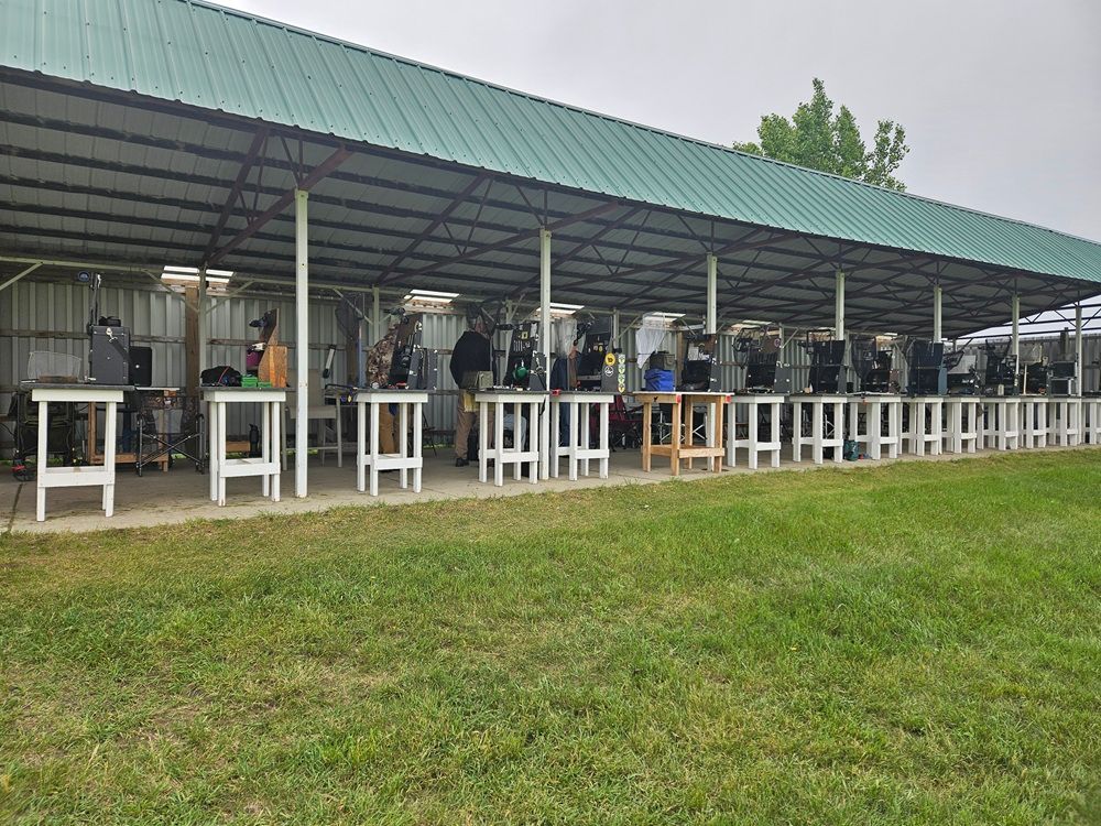 A group of people are standing under a covered area in a field.