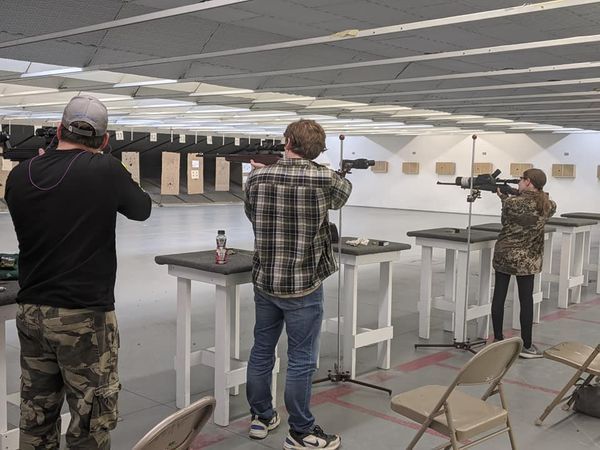 Three people shooting rifles at an indoor shooting range.