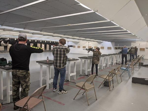 People shooting guns at an indoor shooting range; various stances, aiming at targets.