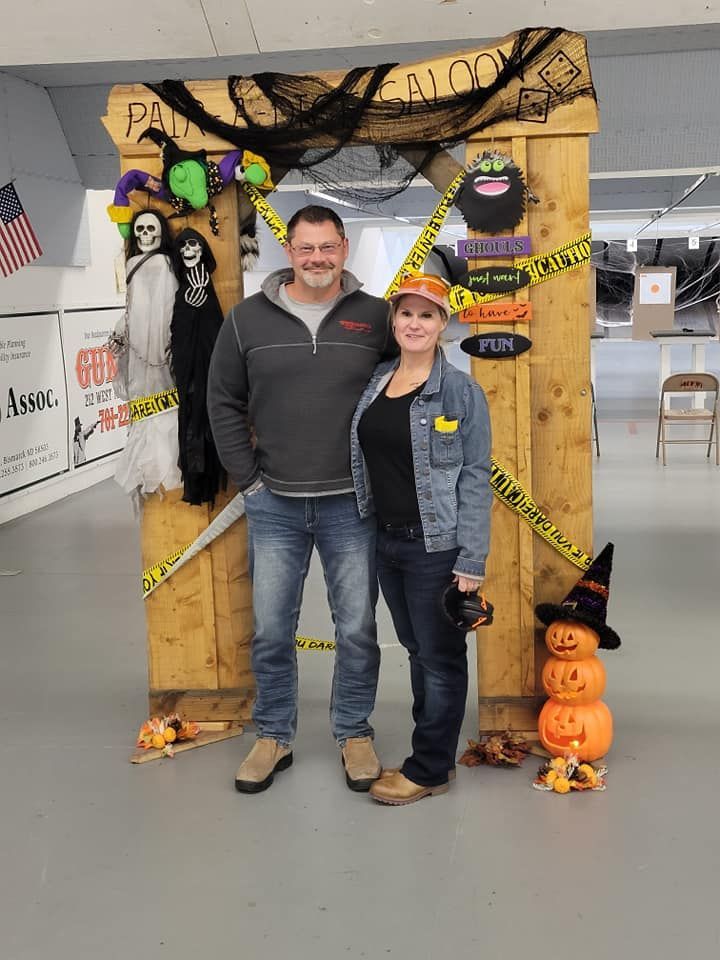 A man and a woman are posing for a picture in front of a wooden frame decorated for halloween.