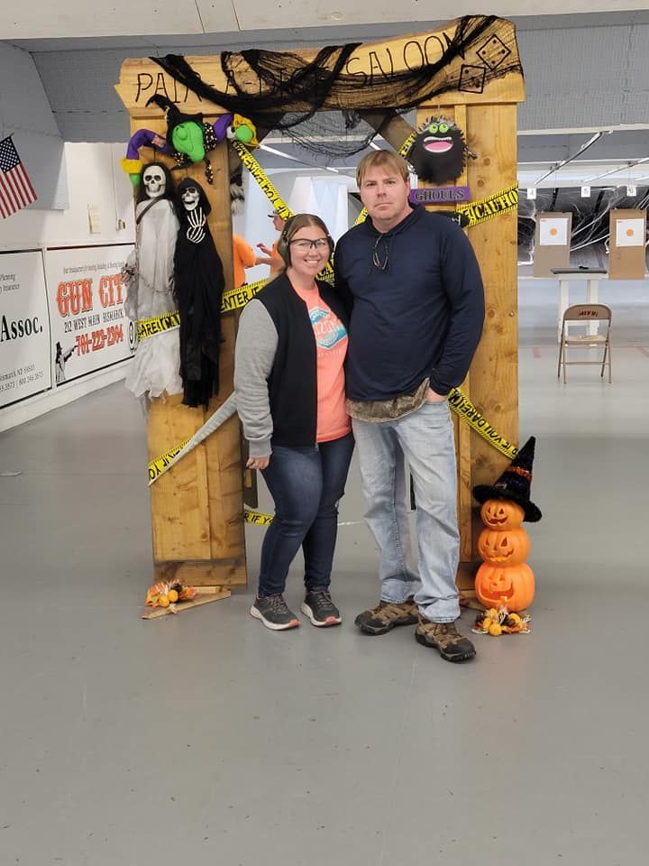 A man and a woman are posing for a picture in front of a wooden frame decorated for halloween.