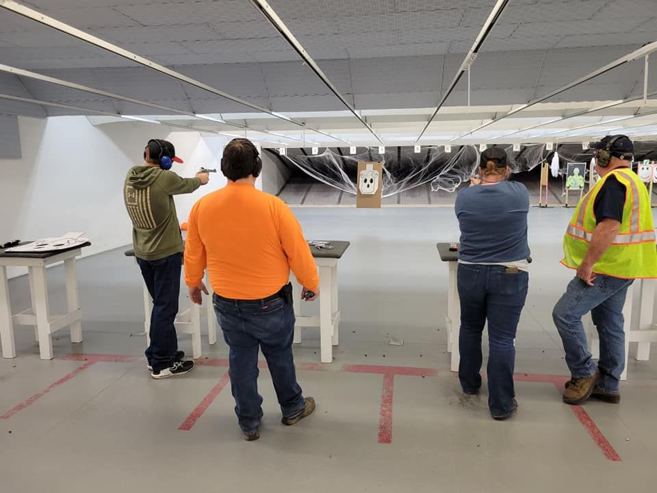 People shooting guns at targets in a shooting range. Concrete floor, metal targets, safety vests, and ear protection.