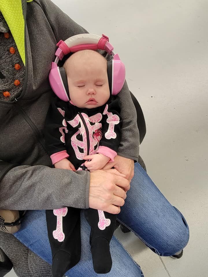 A baby wearing headphones and a skeleton outfit is being held by a person.