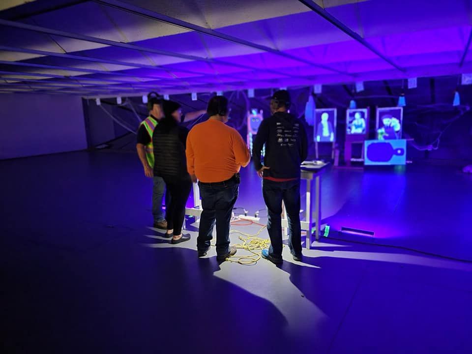 A group of people are standing in a dark room with purple lights.