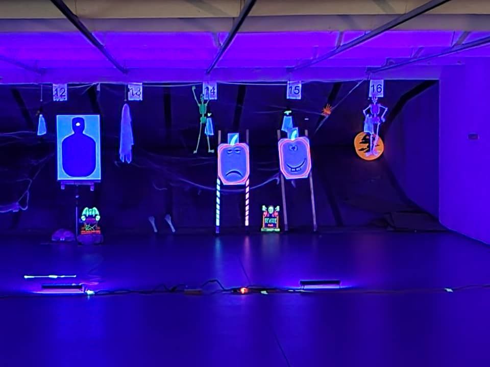 Shooting range with Halloween-themed neon targets under black lights.