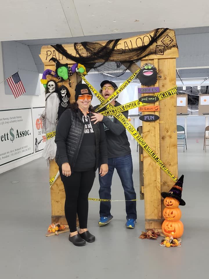 A man and a woman are standing in front of a wooden arch decorated for halloween.