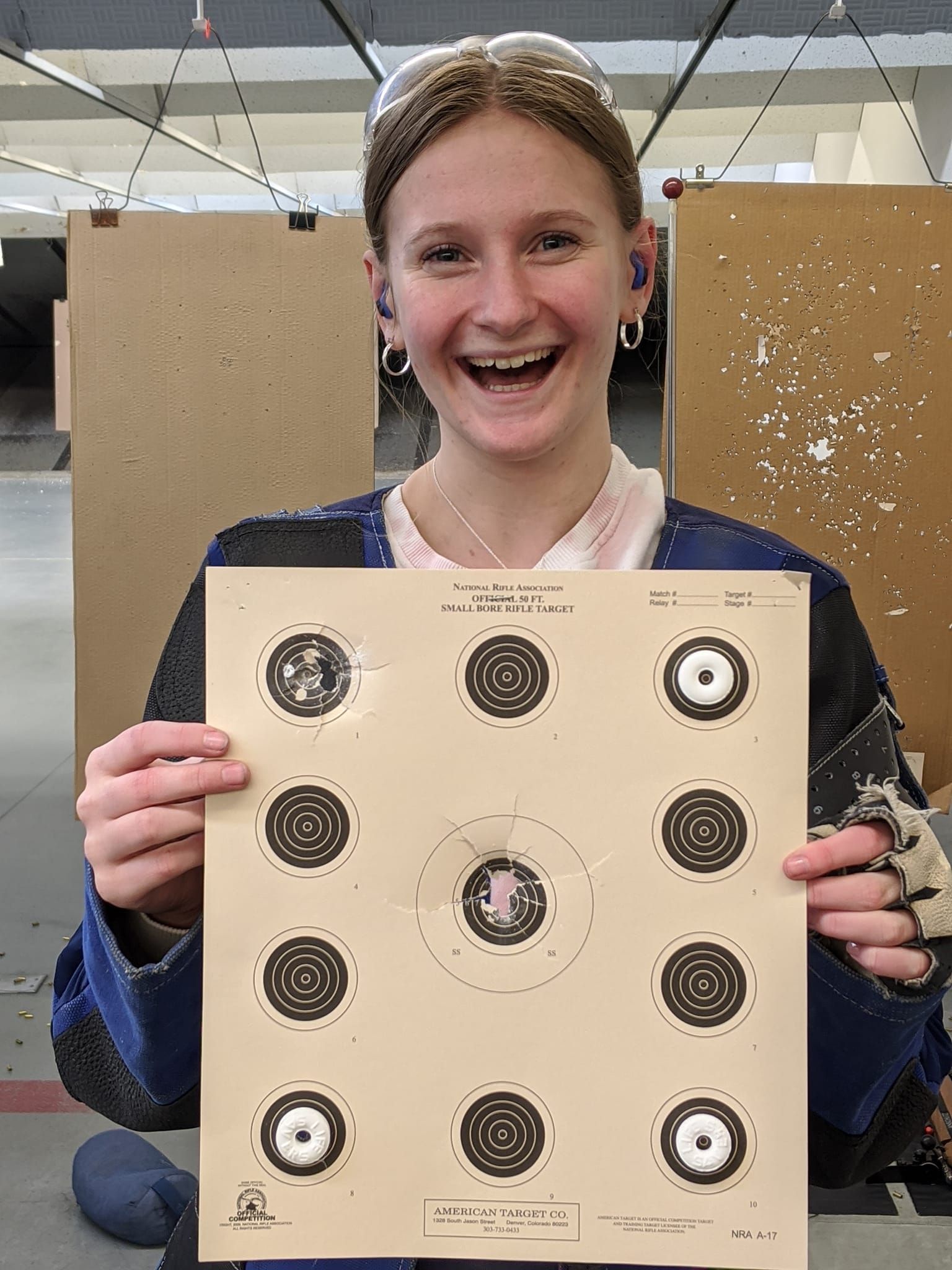 A young woman is holding a target in her hands and smiling.