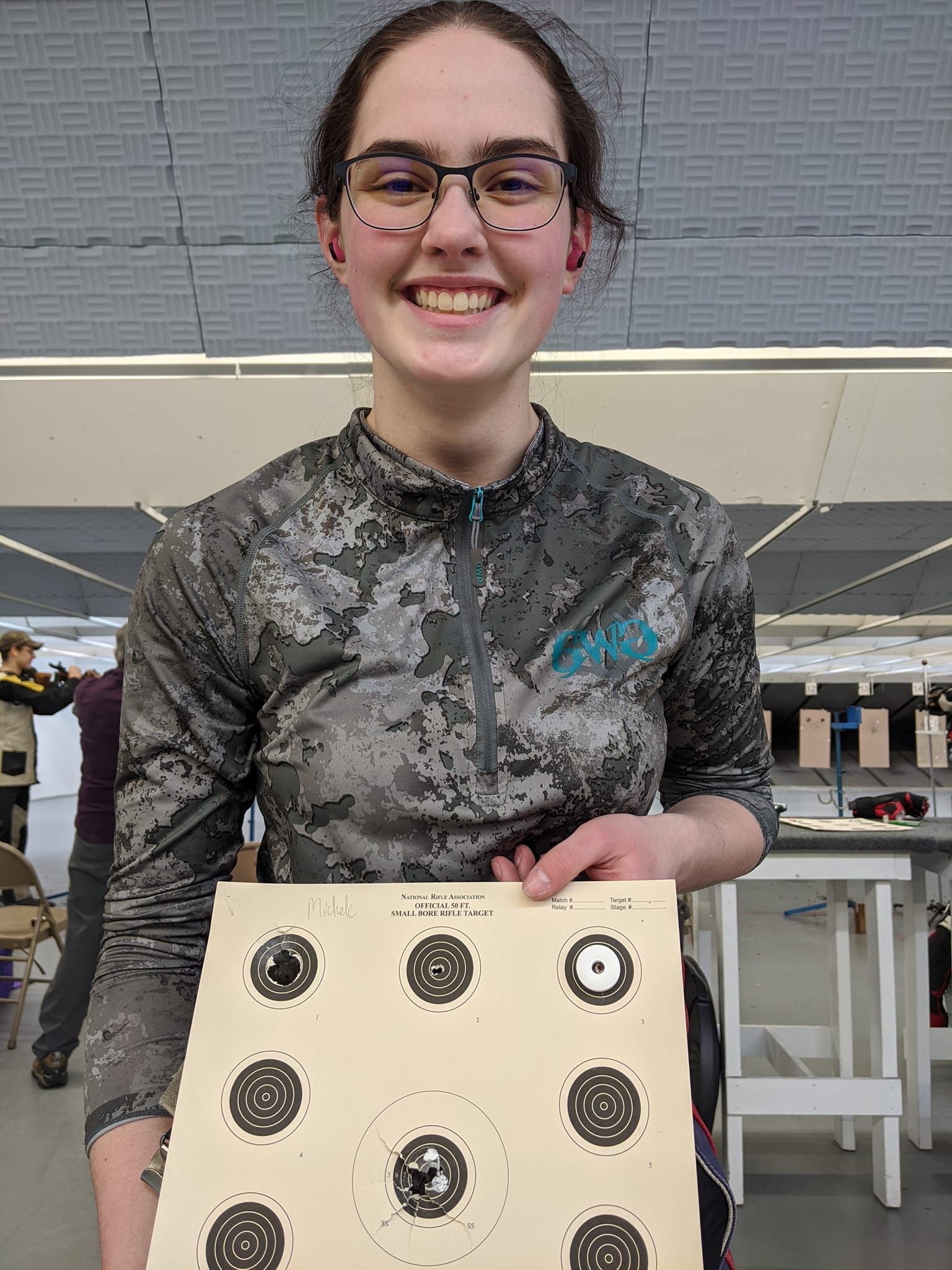 A young woman is holding a target in her hands and smiling.