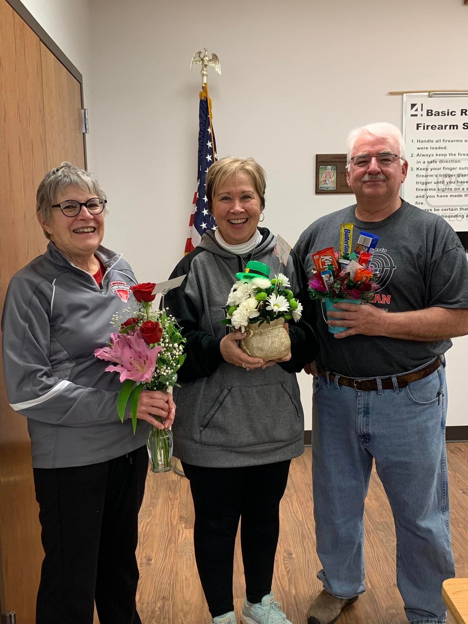Three people are standing next to each other in a room holding flowers.