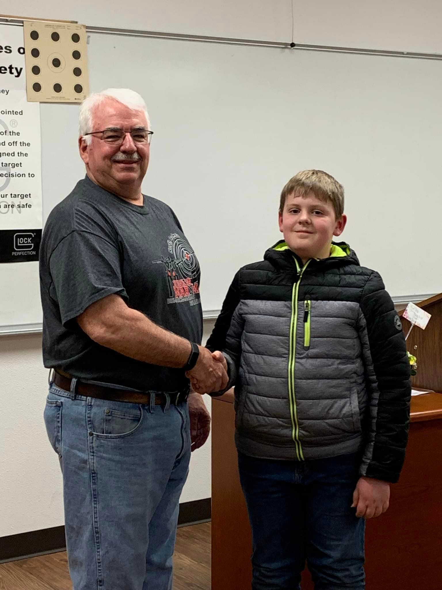 A man and a boy are shaking hands in a classroom.
