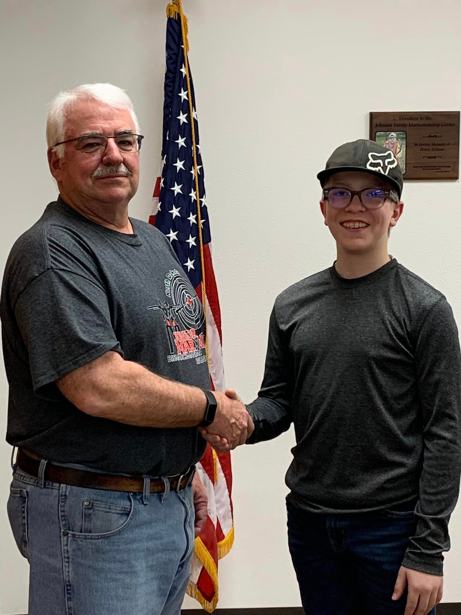 A man and a boy are shaking hands in front of an american flag.