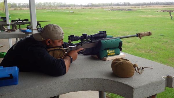 Man aiming a rifle at a shooting range; he is using a green support.