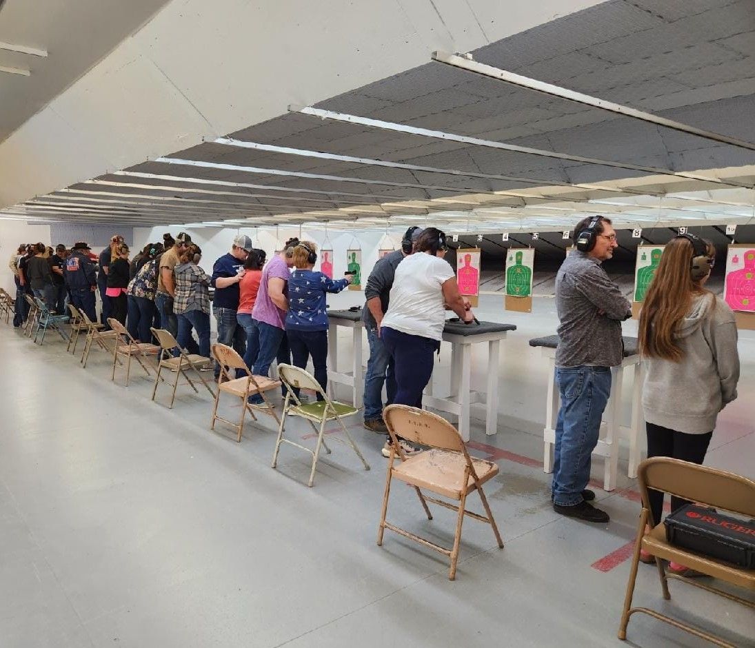 People at a shooting range, aiming at targets. They are wearing ear protection and standing in a line.